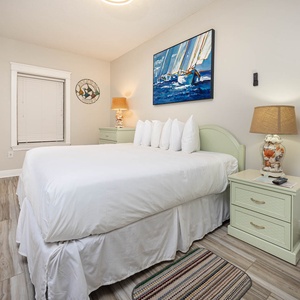 Bright and airy guest bedroom featuring a king bed with plush white linens, coastal artwork, and light green nightstands