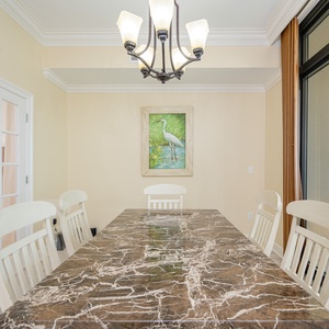 Bright dining area featuring a marble table, white chairs, and a beautiful view through large windows