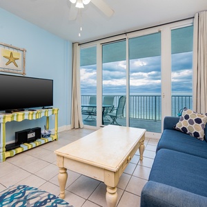 This living area features a large TV, colorful decor, and a stunning beachfront view from the sliding glass doors