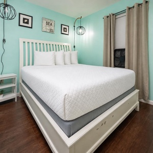 The bedroom features a cozy white bed against a soothing turquoise wall, complemented by stylish decor and natural light