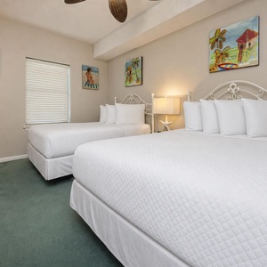 Brightly decorated guest bedroom featuring two double beds with plush bedding, complemented by beach artwork and a lamp