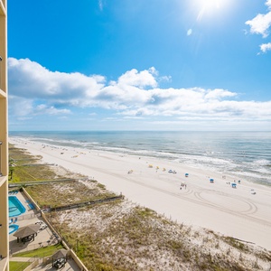 Clear view of the beach front reveals golden sand and colorful umbrellas under a bright blue sky, enhancing the coastal vibe