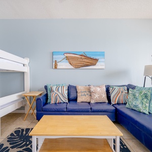 The living area features a beige sofa with a decorative pillow, a blue accent chair, and sliding doors leading to the balcony