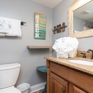 The guest bathroom features a stylish vanity with a granite countertop, neatly arranged towels, and beach decor