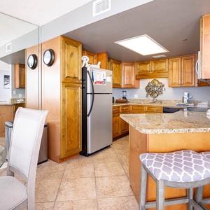 The fully-equipped kitchen features warm wood cabinetry, granite countertops, and a breakfast bar with stylish seating