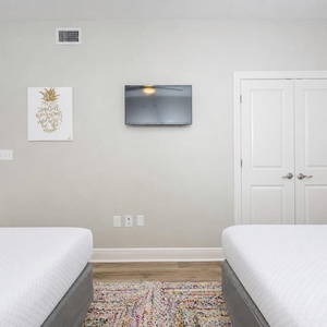 Guest bedroom featuring two queen beds, a wall-mounted TV, and colorful decor with a cozy area rug adding warmth to the space
