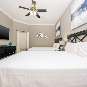 This bedroom features two comfortable queen beds, a wall-mounted TV, and stylish artwork, creating a relaxing retreat