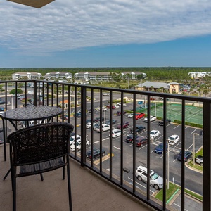 Master balcony featuring a round table and chairs, offering a view of nearby tennis courts and a vibrant parking area below