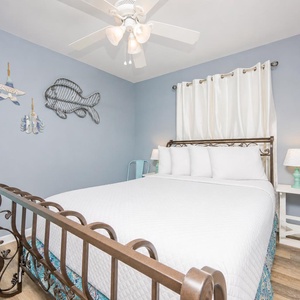 This cozy guest bedroom features a stylish bed, soft blue walls, and charming beach-themed decor for a relaxing stay