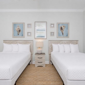 Rest comfortably in this serene guest bedroom featuring two double beds, coastal artwork, and a warm, inviting vibe