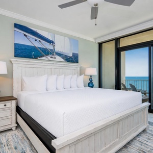 Relax in the master suite featuring a king bed, coastal decor, and beachfront balcony access