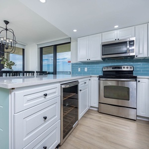 Kitchen features white cabinetry, a sleek countertop, breakfast bar, and wine cooler, complemented by a beach front view