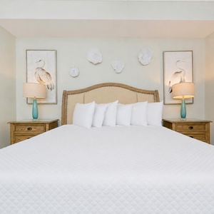 Relax in this inviting master bedroom featuring a king-size bed, elegant decor, and soothing coastal artwork