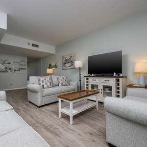 The living area features a comfortable sofa, a large TV, and beach-themed decor, perfect for relaxation