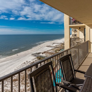 The balcony features stylish seating with panoramic views of the tranquil beach and gentle waves lapping at the shore