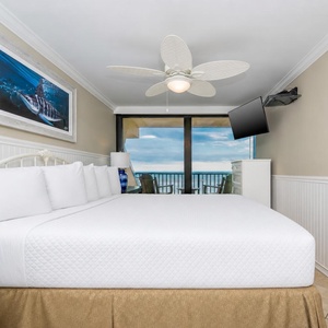 This bedroom features a plush king bed, a mounted TV, and a stunning beachfront view through large sliding glass doors