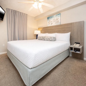 Relax in this comfortable king suite featuring a plush bed, soft lighting, and a mounted TV for entertainment