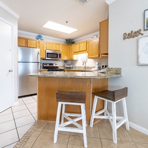 Modern kitchen features wooden cabinetry, granite countertops, and a breakfast bar with two stools for casual dining
