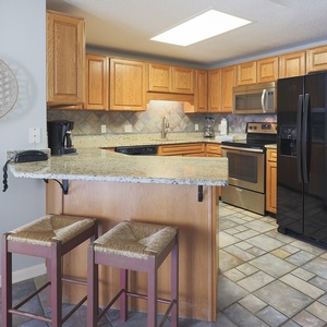 Warm wood cabinetry complements the granite countertops in this inviting kitchen, featuring a breakfast bar with two stools