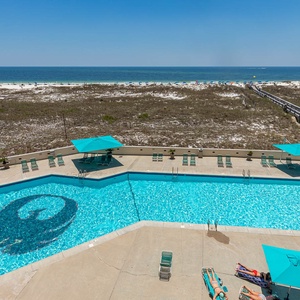 Inviting pool area features turquoise umbrellas and lounge chairs, with a view of the beach just beyond the lush dunes