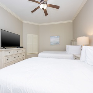 This guest bedroom features two comfortable queen beds, a flat-screen TV, and soft neutral tones for a relaxing stay