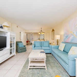 This inviting living area features soft blue seating, a TV, and a view of the kitchen, perfect for relaxation and gatherings