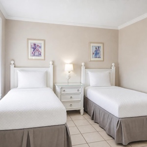 Light-filled guest bedroom featuring two twin beds with white linens, a nightstand, and charming artwork on the walls