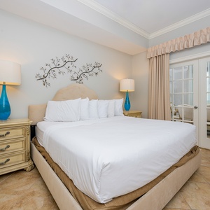 The master bedroom features a plush king bed, elegant decor, and a charming view through glass doors leading to a dining area