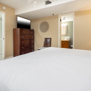 The bedroom features a king bed, a wooden dresser, a TV, and an adjoining bathroom visible through a doorway