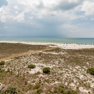 Expansive view of the beach with white sand and colorful umbrellas, framed by lush greenery and a winding path to the shore