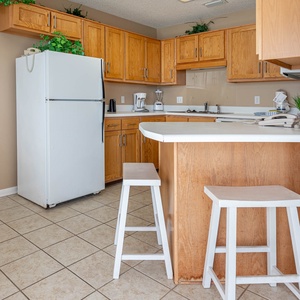 Bright kitchen area featuring wooden cabinets, a white refrigerator, and a breakfast bar with two stools for casual dining