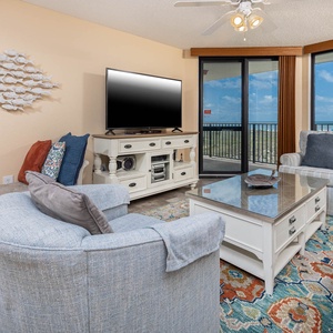 Cozy living area features a large TV, comfortable seating, and a balcony with views of the beach and gulf beyond