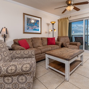 The living area features comfortable seating, a rustic coffee table, and a stunning beach view through the large balcony door