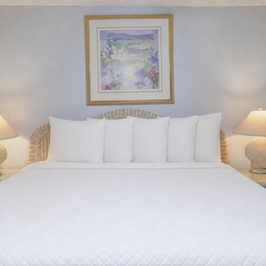 Cozy bedroom featuring a large king bed with white linens, complemented by shell-themed lamps and a floral artwork above