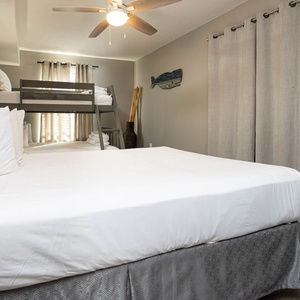 This guest bedroom features a queen bed with a gray skirt and a twin over full bunk bed illuminated by natural light
