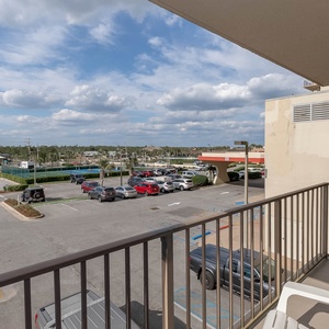 The balcony offers a view of the parking area and nearby amenities from the master under a partly blue sky