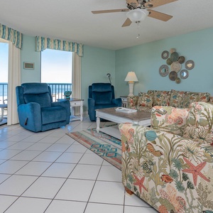 The living room features vibrant floral-patterned sofas, cozy blue recliners, and a view of the beach