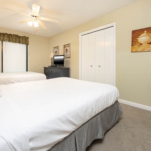 Guest bedroom featuring two queen beds, a dresser with a TV, and a cozy plant accent for a welcoming atmosphere