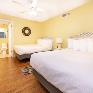 Bright yellow walls complement two double beds with white linens, creating a cheerful guest bedroom with a cozy atmosphere