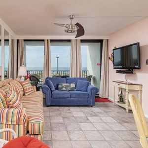This living area features colorful striped sofas, a TV, and a view of the beach through large windows