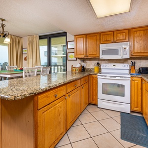 Bright wooden cabinetry and coffee station complement the granite countertops in this kitchen with a view of the balcony