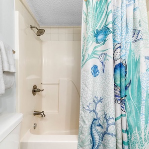 Guest bathroom features a tub/shower combo with a colorful aquatic-themed shower curtain and plush white towels nearby