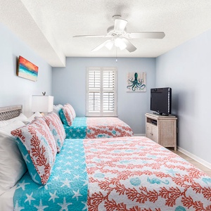 Bright guest bedroom featuring two double beds, a TV, and coastal-inspired decor