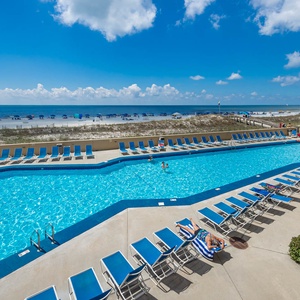 The inviting pool area features blue lounge chairs, with guests enjoying the refreshing water and a scenic beach view beyond