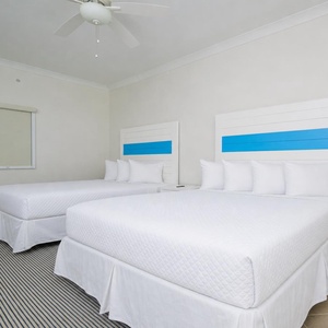 Rest comfortably in this guest bedroom featuring two queen beds, stylish blue accents, and a soft area rug