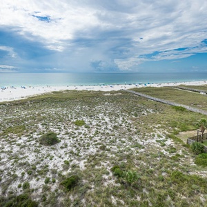 Expansive view of the beach with white sand, dotted with colorful umbrellas and lounge chairs under a bright sky