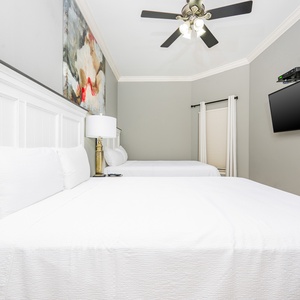 This guest bedroom features two comfortable queen beds, a wall-mounted TV, and a stylish artwork above the headboard