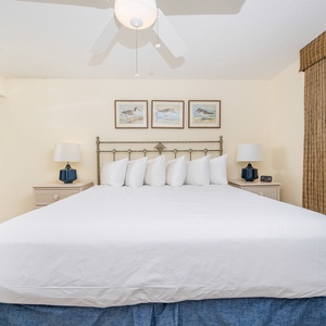Relax in this master bedroom featuring a king bed, coastal artwork, and a view of the beach balcony