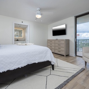 The master suite features a plush king bed, a sleek dresser, and a cozy chair, with a view of the balcony