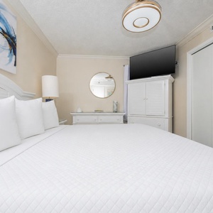 Elegant bedroom featuring a king bed with plush pillows, a mounted TV, and stylish white furnishings